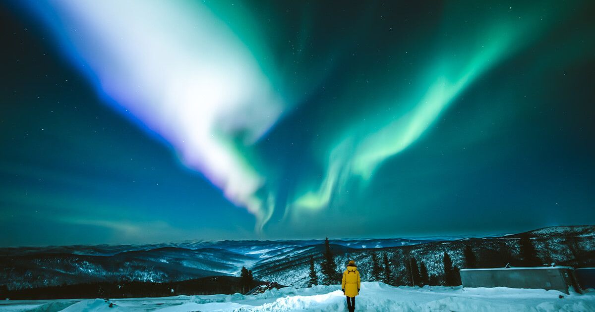 Person in a yellow jacket in Alaska looking at the Northern lights (Aurora Borealis)