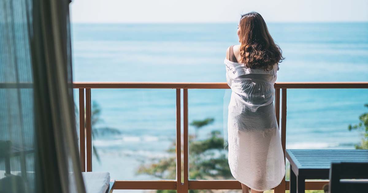 Woman standing on balcony looking out to blue water on luxury vacation.
