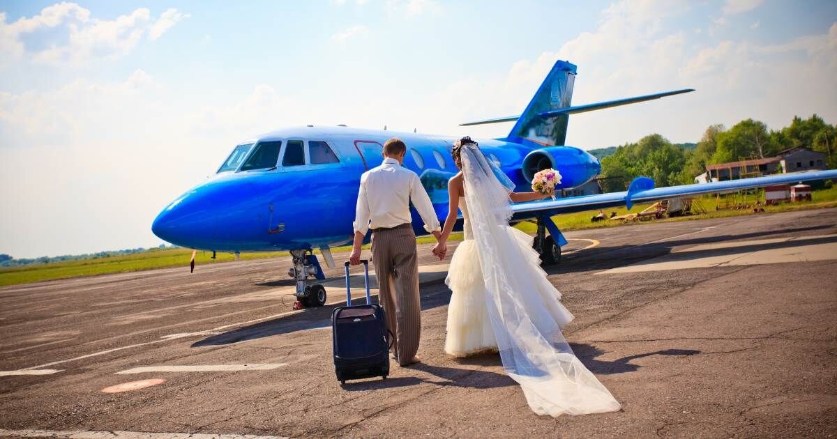 bride and groom holding hands walking towards a plane 